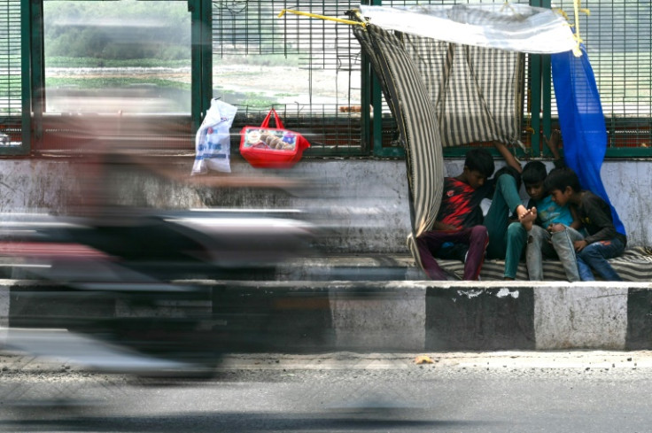 Boys sit beneath a makeshift canopy along a street on a hot summer day in New Delhi