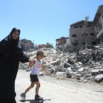A woman and a girl walk past buildings destroyed during previous Israeli strikes on the southern Lebanese village of Aita al-Shaab, on June 29, 2024