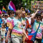 Marchers in tie-dyed t-shirts hold a sign reading "Protect trans healthcare."