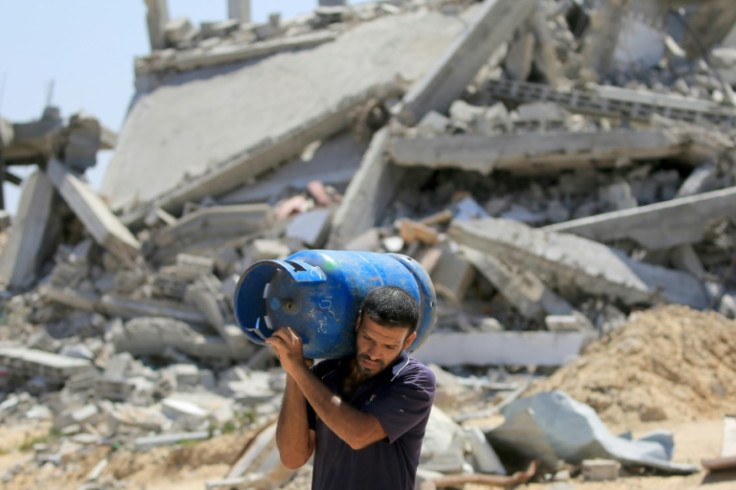 A Palestinian man carries a gas bottle on his shoulder past buildings destroyed in the Israeli bombardment of Khan Yunis, in the southern Gaza Strip