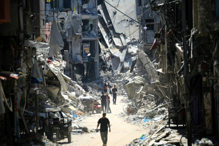 Palestinians walk along a narrow street past destroyed buildings in Khan Yunis, in the southern Gaza Strip, on June 11, 2024