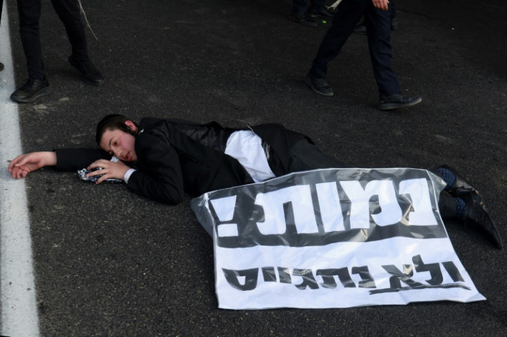 A young Orthodox Jew lies on the road near a banner written in Hebrew "We will die and no draft" in Bnei Brak