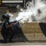 A Bangladesh policeman fires tear gas shells at protesters during clashes in Dhaka