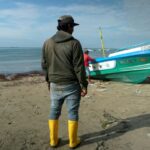A fisherman looks at a colleague painting a boat on the beach at the Santa Rosa fishing port in Salinas, Ecuador, in June 2024