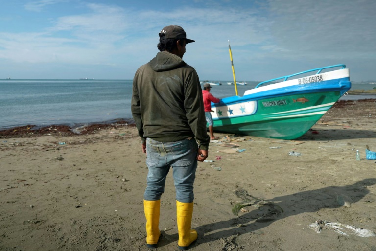 A fisherman looks at a colleague painting a boat on the beach at the Santa Rosa fishing port in Salinas, Ecuador, in June 2024