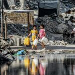 Girls walk with water containers past destroyed buildings and open sewage in Khan Yunis in the southern Gaza Strip on July 8, 2024