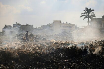 A Palestinian youth walks past piles of smouldering waste at Al-Maghazi Palestinian refugee camp, central Gaza, in the absence of municipal services during the Israel-Hamas war