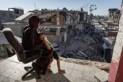 A member of Ibrahim Abu Alya's family sits with a child on the balcony of her house heavily damaged by Israeli bombardment, in the town of Bani Suheila near Khan Yunis, southern Gaza