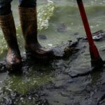 A fisherman with boots covered in oil stands on a contaminated shore of Lake Maracaibo in Venezuela, on July 11, 2024