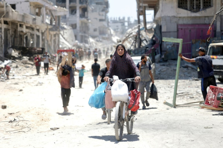 A Palestinian woman rides a bicycle past destroyed buildings in the Shujaiya neighbourhood of Gaza City on July 11, 2024
