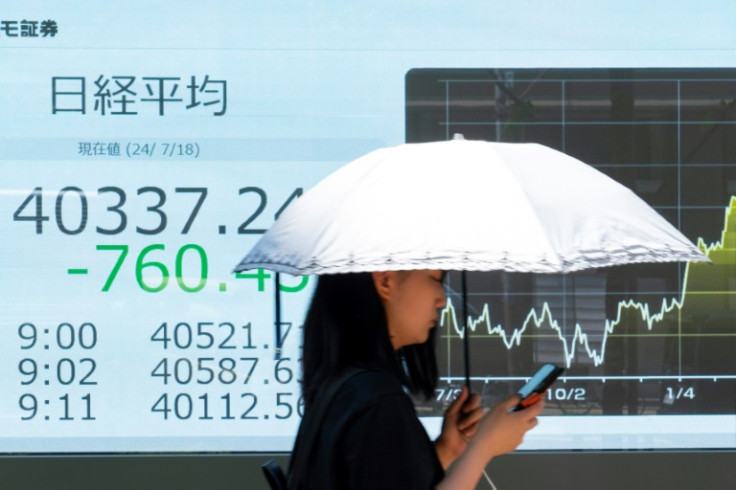 A woman walks past an electronic board displaying Tokyo Stock Exchange prices