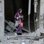 A woman checks her phone amid the rubble of a building destroyed by Israeli bombardment in Gaza City's Sheikh Radwan district