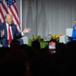 Donald Trump sitting on stage at a panel in front of American flag