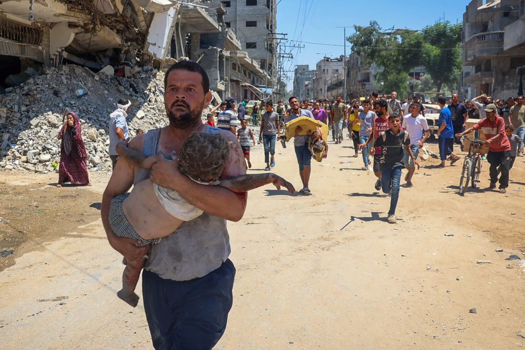 A man carries an injured child, fleeing down a road in al-Bureij refugee camp in the central Gaza Strip.