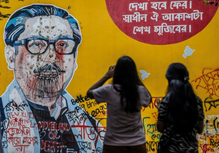 People photos in front of anti-government graffiti on a vandalised mural depicting Bangladesh's founding father Sheikh Mujibur Rahman days after a student-led uprising ended the 15-year rule of his daughter Sheikh Hasina