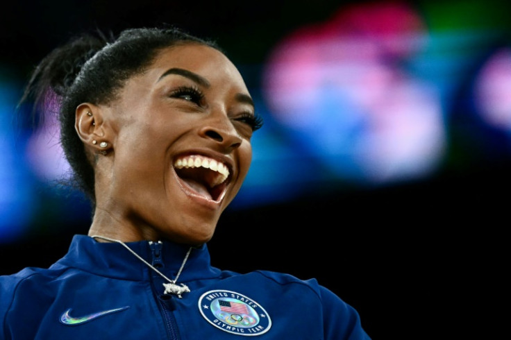 Simone Biles poses with her goat necklace during the podium ceremony after winning the women's gymnastics all-around title at the Paris Olympics