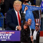 Republican presidential nominee former president Donald Trump holds an artwork of the assassination attempt, which he signed for the artist, during a campaign rally at the Georgia State University Convocation Center on August 3, in Atlanta.