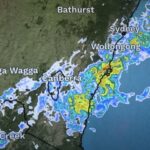 Digital weather forecast screen showing multi-day outlook with temperature highs and lows, rainfall predictions, and animated icons for sun, clouds, and storms across Sydney and surrounding regions.